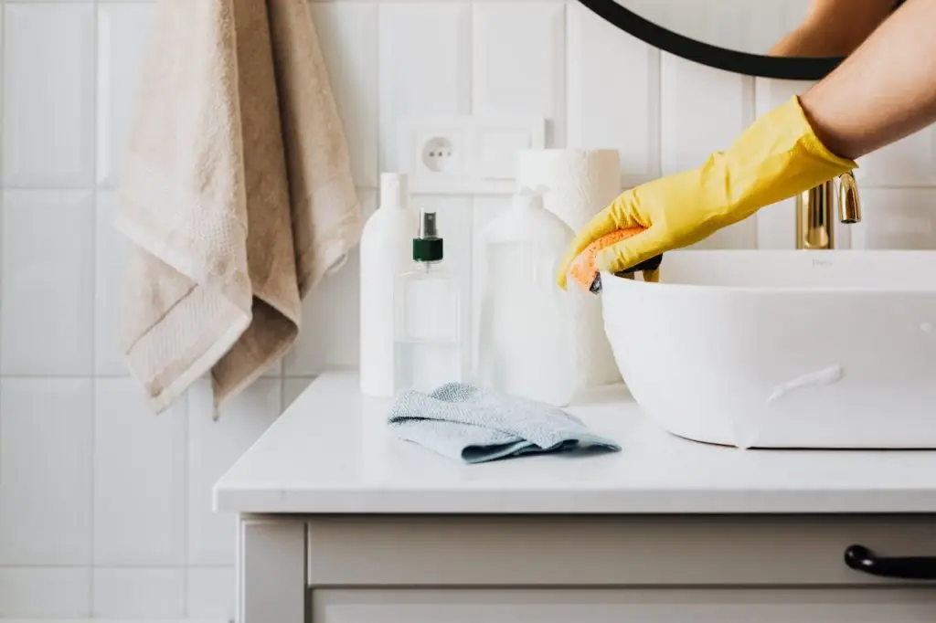 pexels-photo-4239113 Person cleaning a bathroom sink with yellow gloves and cleaning products on a countertop.
